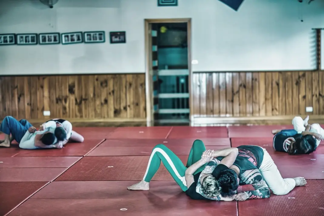 Club members practising groundwork on the red mats, with the dojo's timber panelling and framed photos behind them.